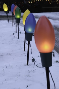 String of large holiday lights on posts along suburban driveway (focus on near blue bulb)-1